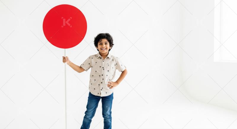Cheerful boy presents big red circle sign on white background.
