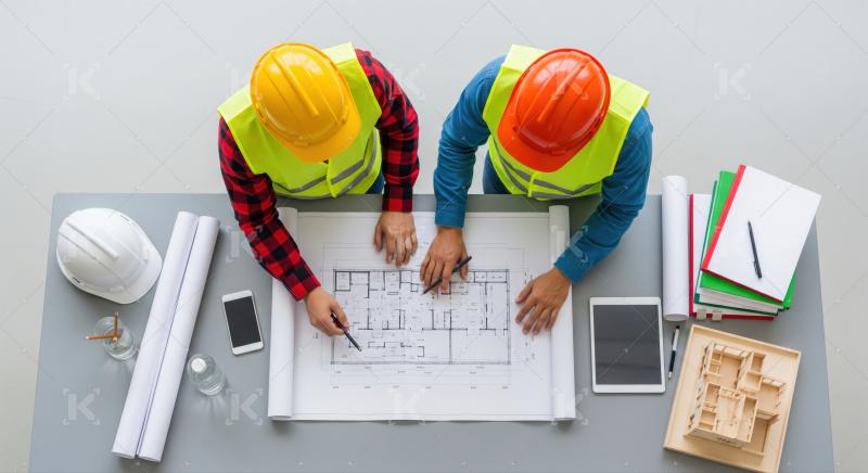Two professionals meticulously review building plans, focusing on project details.