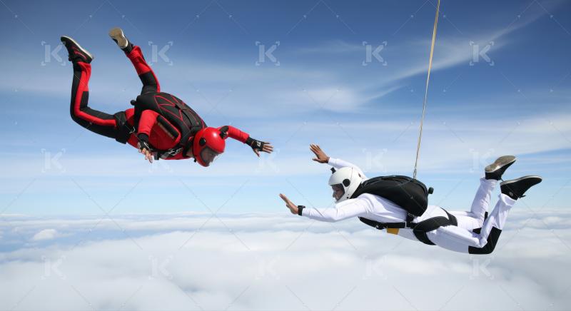 Two skydivers freefalling above clouds reaching out to each other.