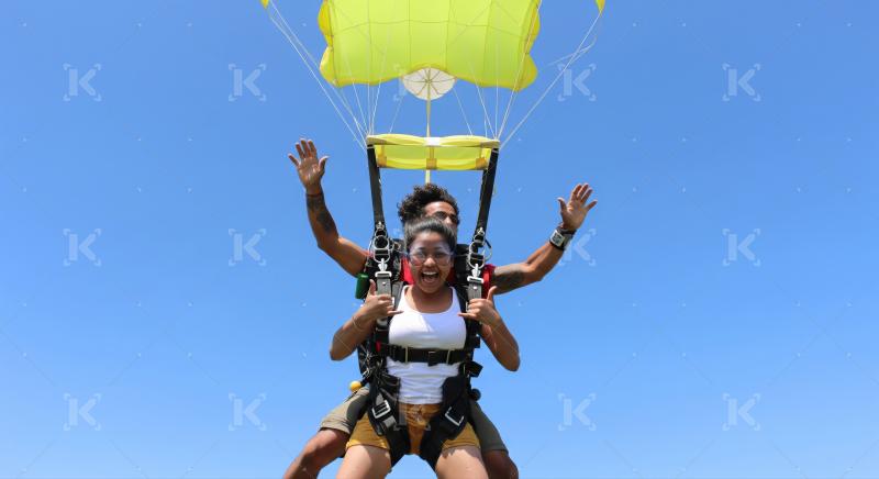 Two happy individuals enjoy thrilling tandem skydive against blue sky.