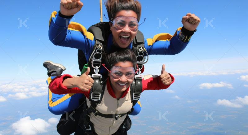 Two happy women enjoy exhilarating tandem skydive high above clouds.