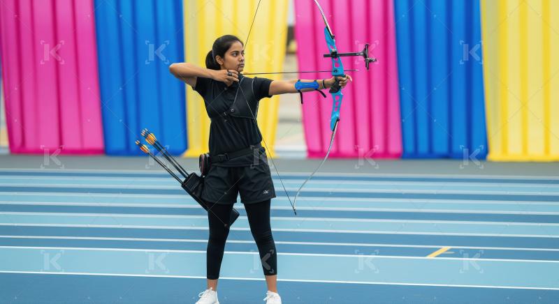 Young Woman Archer Aiming Bow and Arrow on Blue Track