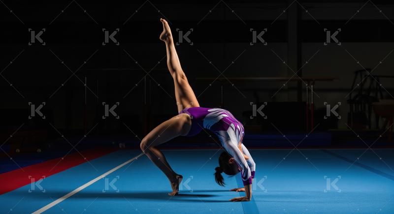 Female Gymnast Performs Artistic Back Bend Pose in Dark Gymnasiu