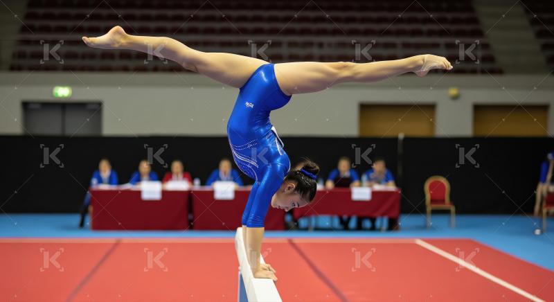 Female Gymnast Performs Handstand Split on Balance Beam with Pre
