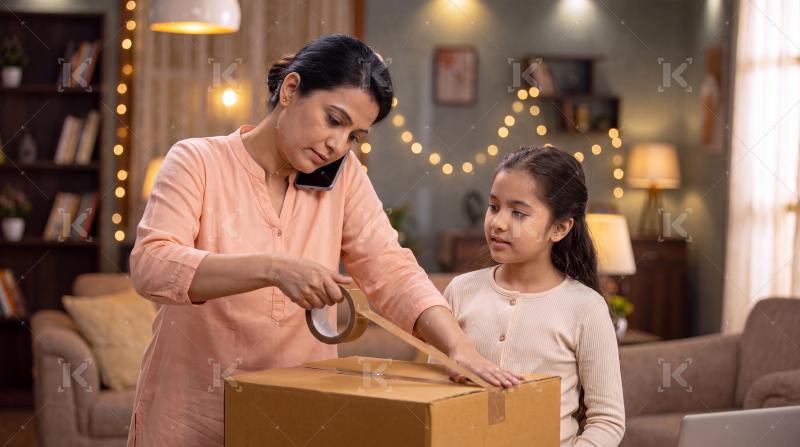 Happy indian mother and daughter packing cardboard box together at home