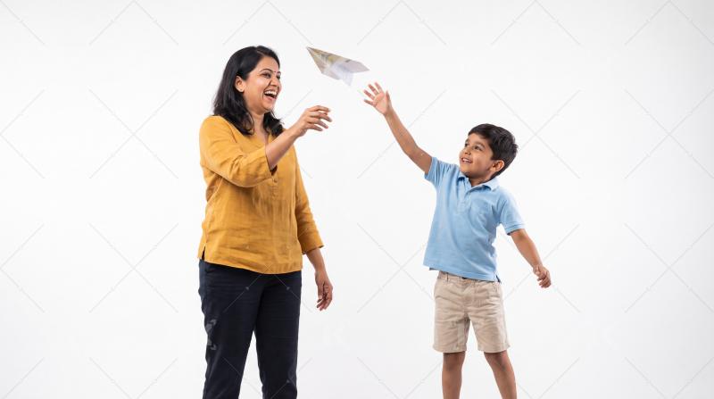 Happy indian mother and son playing with paper toy plane on white background