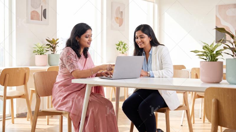 Two young indian women using laptop together sitting at cafe