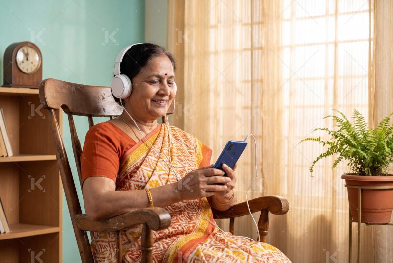 Senior indian woman sitting on sofa using smartphone