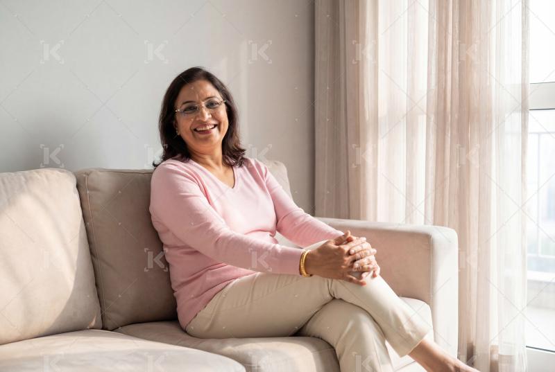 Happy indian senior woman sitting on sofa at home