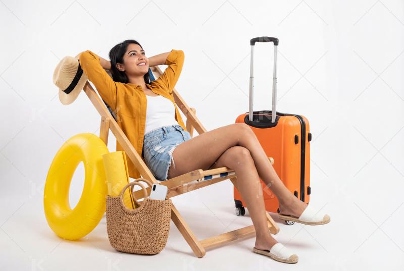 Happy indian woman relaxing on a wooden lounge chair surrounded by travel items