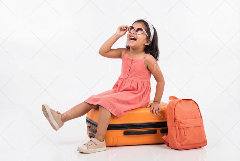 Happy little indian girl sitting with travelling bag on white background
