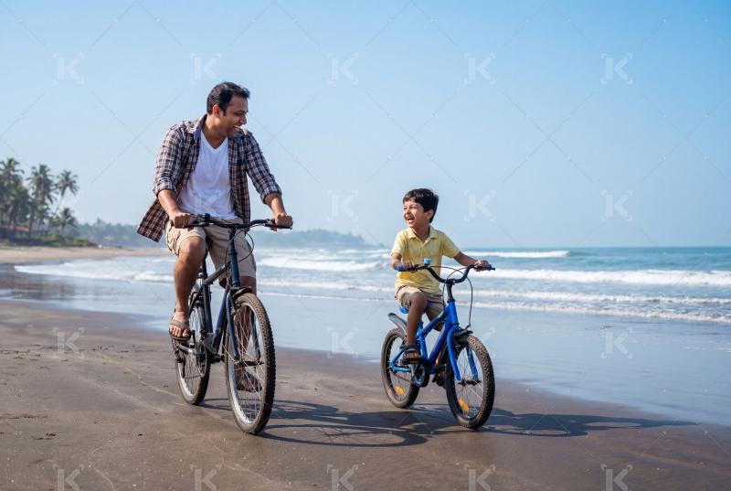 Happy indian father and son riding cycles at beach