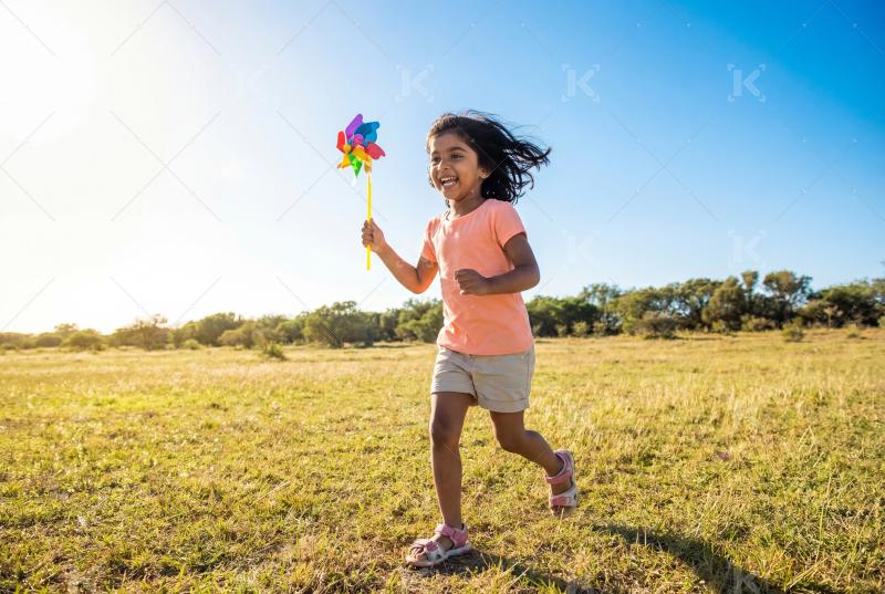 Happy indian girl holding pinwheel enjoying at field