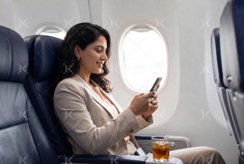 Young indian business woman using smartphone sitting in plane