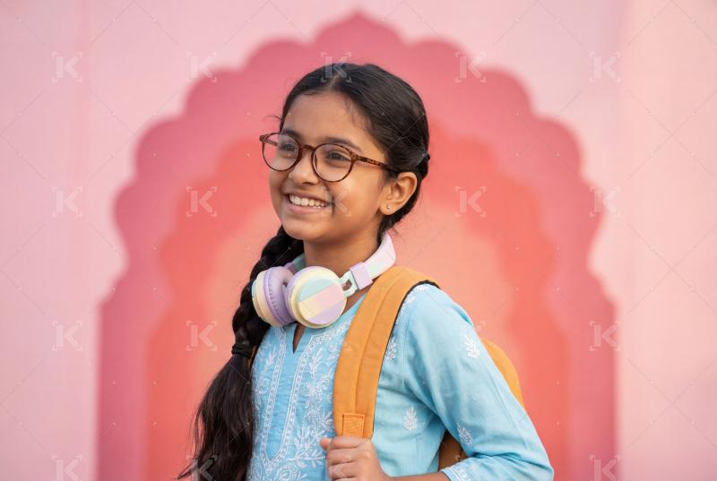 A cheerful young student with glasses, headphones, and a backpac