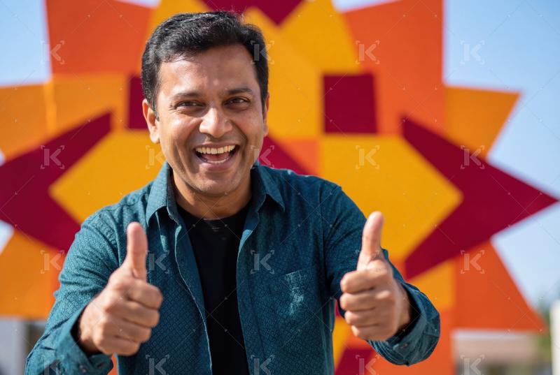 A cheerful man smiling brightly and giving a double thumbs-up ge