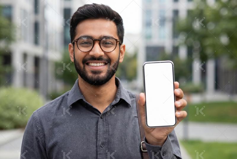 A smiling young man holds up a smartphone with a blank screen, s