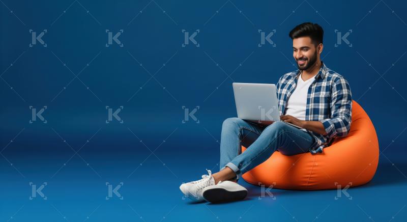 Young Man Happily Using Laptop on Bean Bag Chair