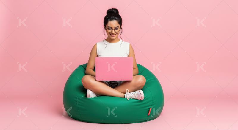 A young woman sits cross-legged on a green bean bag with a pink