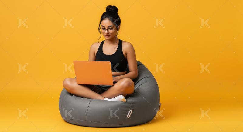 A young woman sits cross-legged on a gray bean bag with an orang