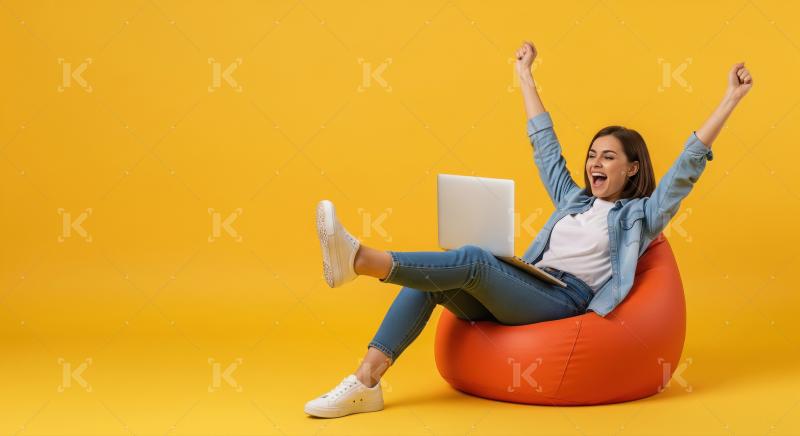 A young woman sitting on an orange bean bag with a laptop joyful