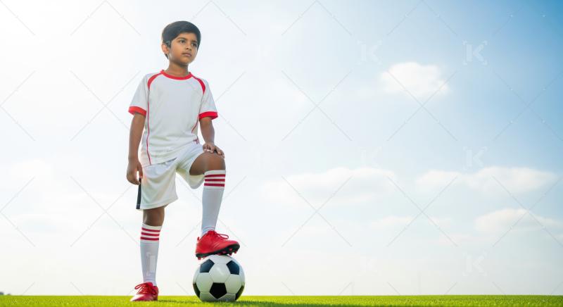 Confident young boy, soccer player, on field, blue sky.