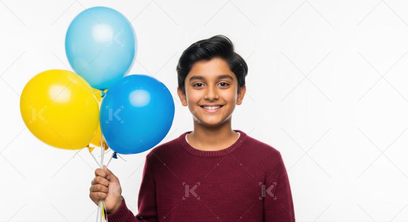 Indian boy sweater holds bright blue and yellow balloons against a plain white background.