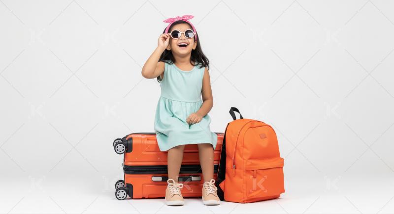 A cheerful young girl in a mint green dress and pink bow sits on