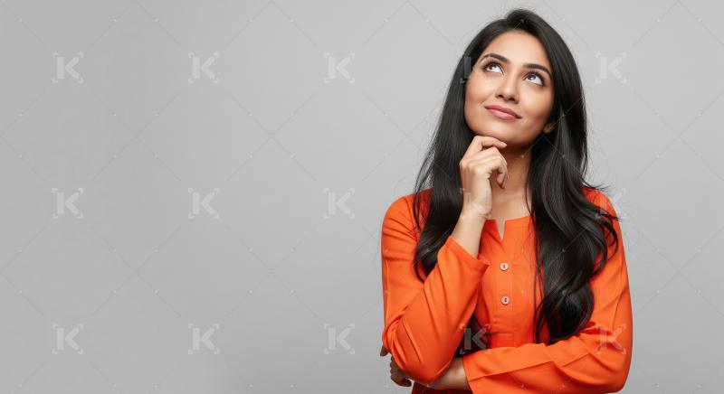 A thoughtful young Indian woman in an orange top stands with her