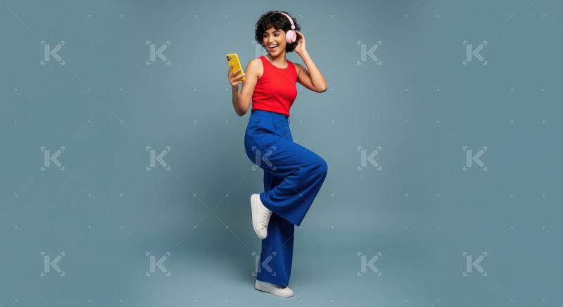 Cheerful woman enjoying music with headphones and smartphone, bl