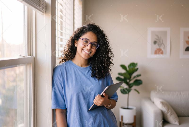 Happy young indian woman holding tablet standing at home