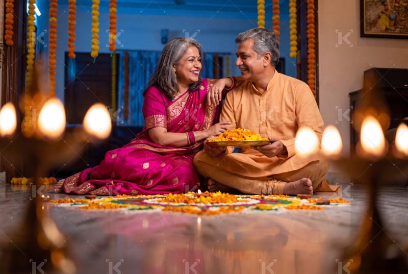 Happy indian senior couple holding flowers plate sitting together on traditional diwali festival at home