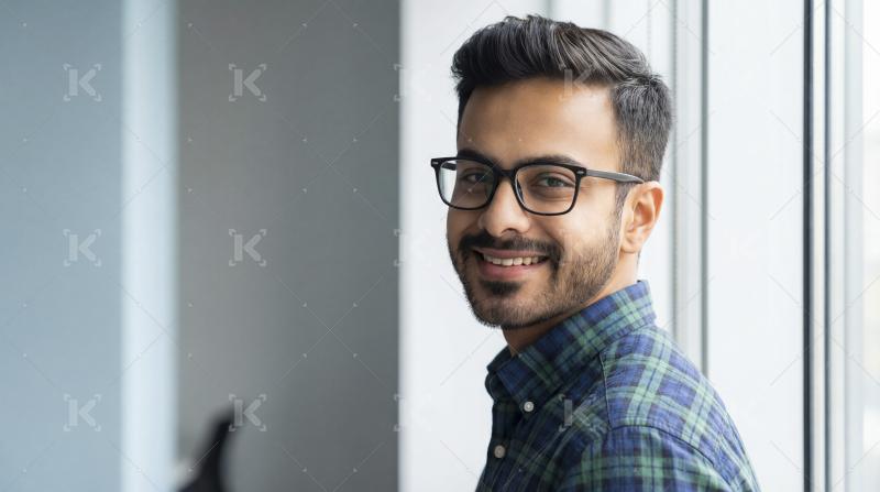 Smiling young Indian man wearing glasses looks back confidently