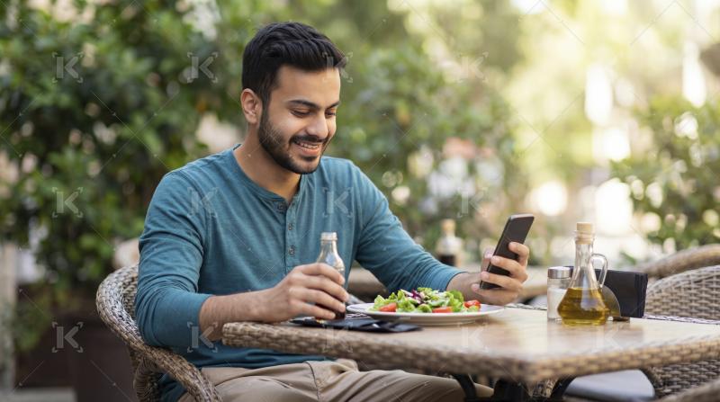 Smiling Man Eating Salad and Using Phone at Outdoor Cafe