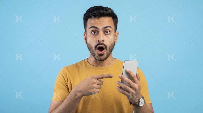 Surprised Young Man Points at Smartphone with Shocked Expression