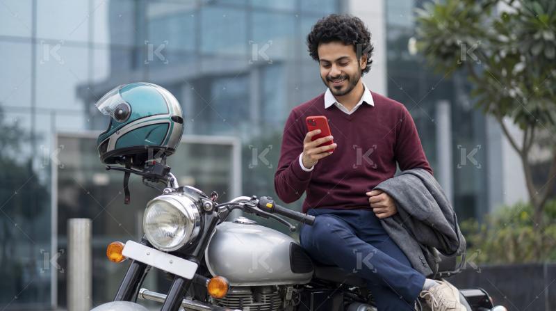 Young Indian Man Smiling, Using Smartphone While Sitting on Moto