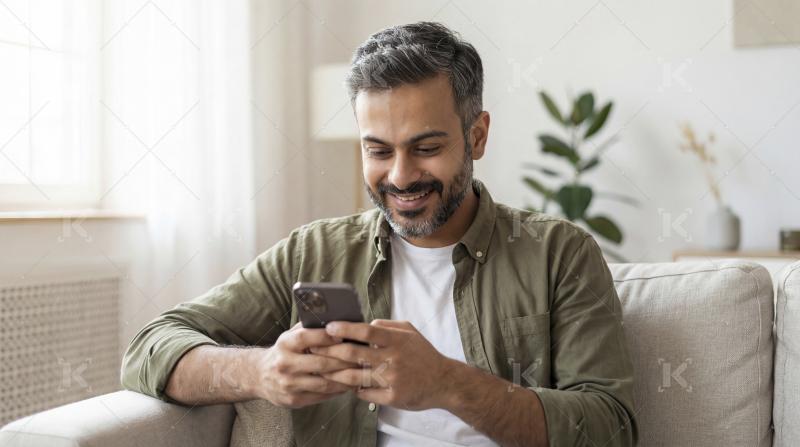 Joyful Man Using Mobile Phone on Sofa at Home