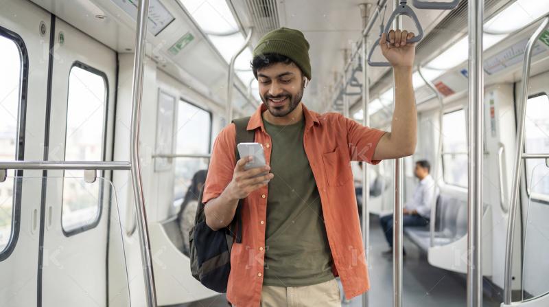 Happy man using smartphone with earbuds while riding subway trai