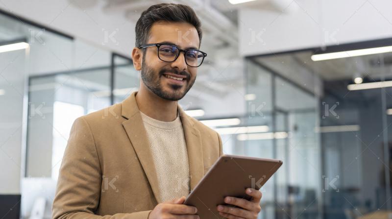 Confident Indian Businessman Smiles Holding Tablet in Modern Off