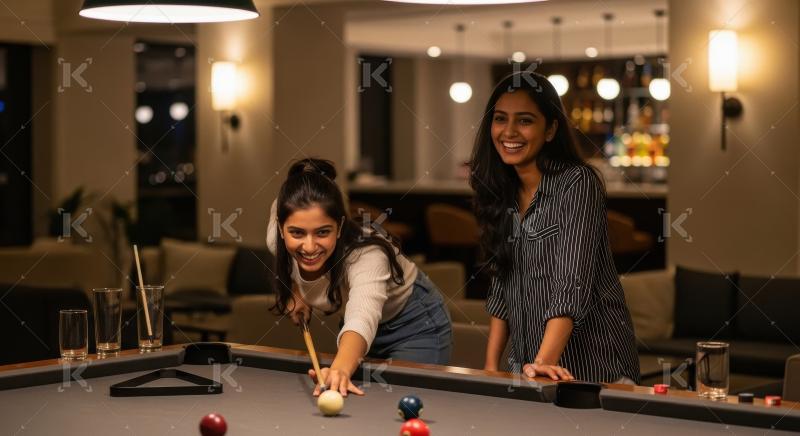 Two young indian female friends playing billiards game together