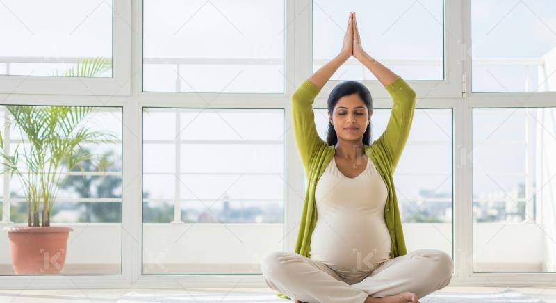 Indian pregnant woman practices yoga art home sitting cross legg
